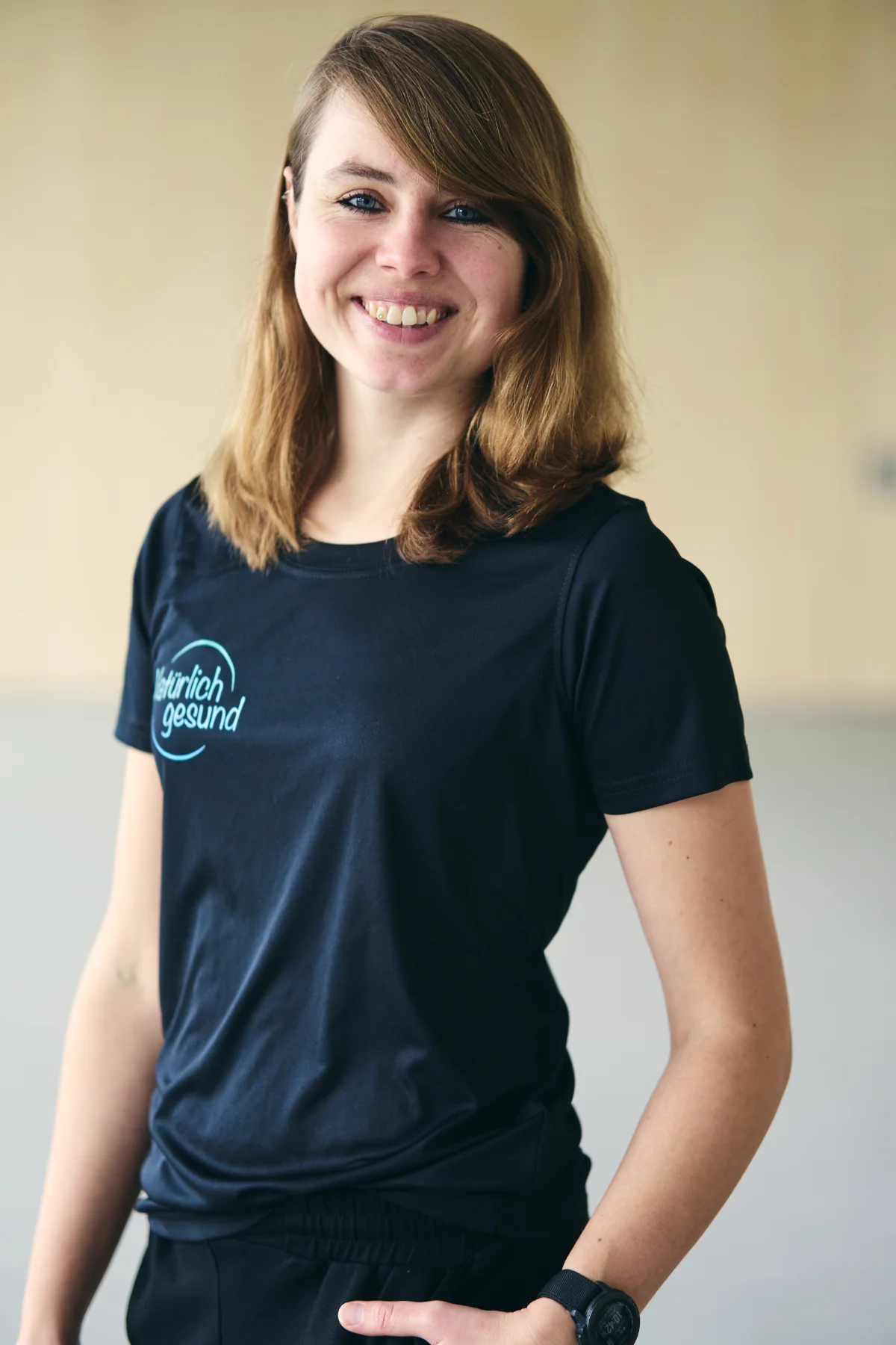 Tahnee Boderius Gesundheitscoach Tahnee Boderius, Sport- und Bewegungstherapeutin mit Bachelor in Gesundheitsmanagement, steht lächelnd in ihrem Praxisraum in Kiel
